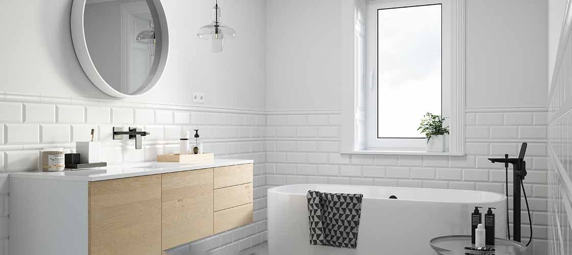 Ljust badrum med vitt kakel. Badrummet har en rund spegel på väggen, ett badkar och en kommod med trälådor.