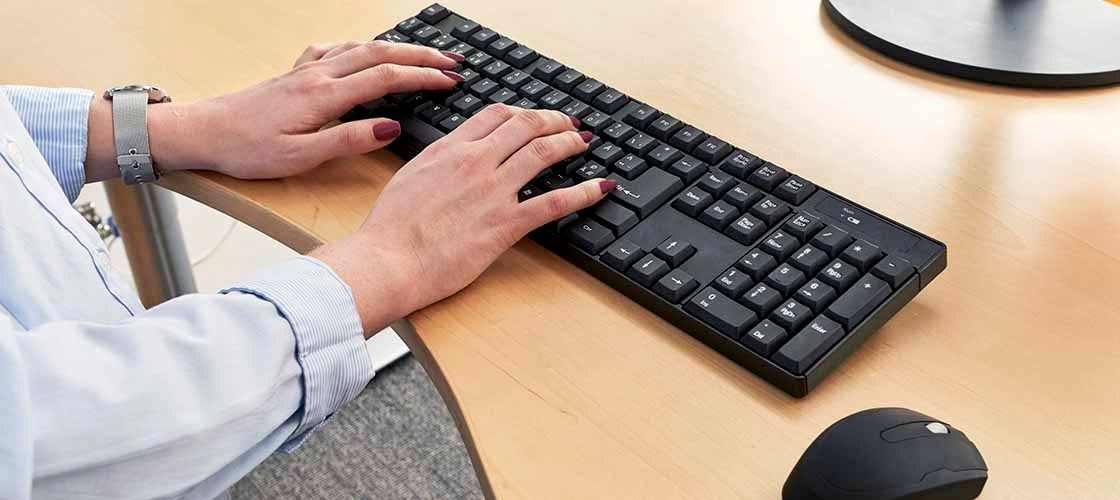 Ett par kvinnliga händer arbetar på ett svart tangentbord. På vänster arm har kvinnan på sig en silvrig klocka. Till höger på bordet ser man delar av en datormus.
