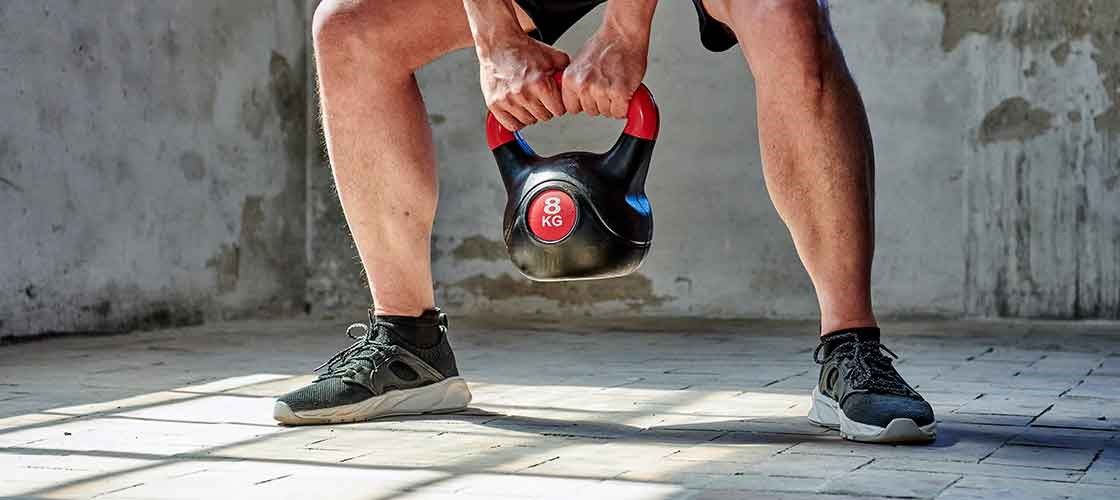 A person performs a squat while holding an 8 kg kettlebell on a bright training floor.