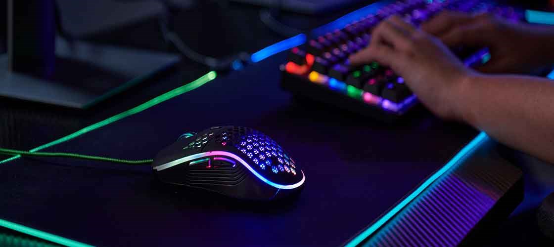Gamingmus med RGB-belysning på ett skrivbord bredvid ett upplyst speltangentbord.
