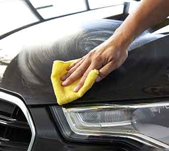 Närbild på en hand om torkar av en svart motorhuv med en gul trasa.