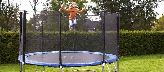 A girl happily bounces on a trampoline with a safety net in a garden.