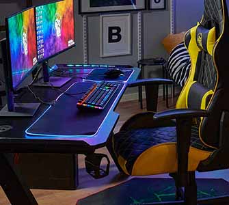 A dark gaming room with a colorful computer screen, with a yellow and black gaming chair in front of it.