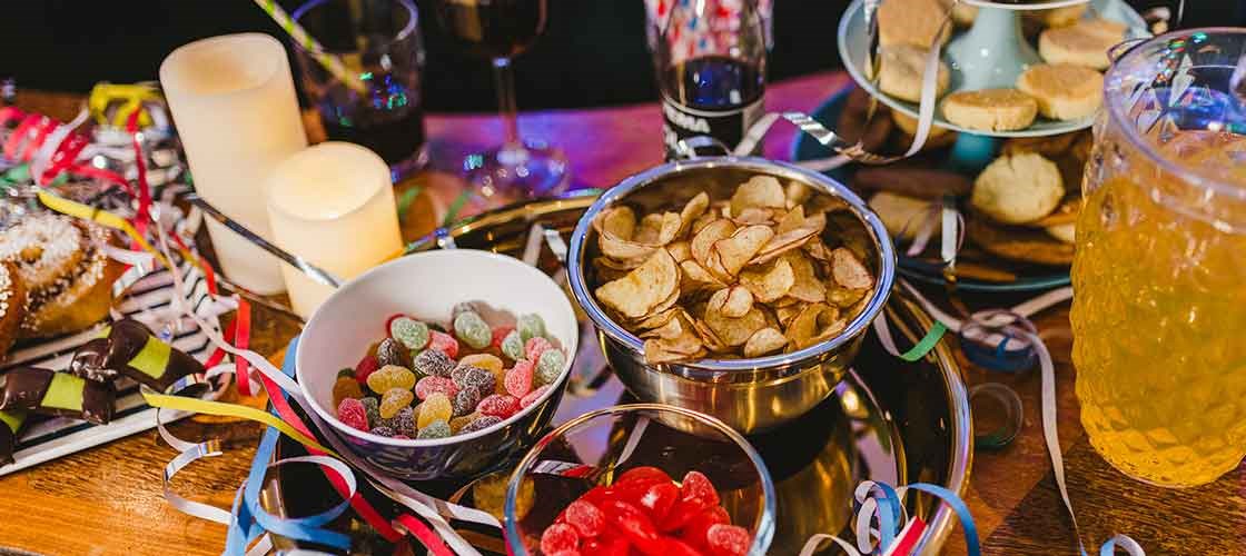 Nyårsbord med chips, godis, drycker, ljus och färgglada serpentiner.