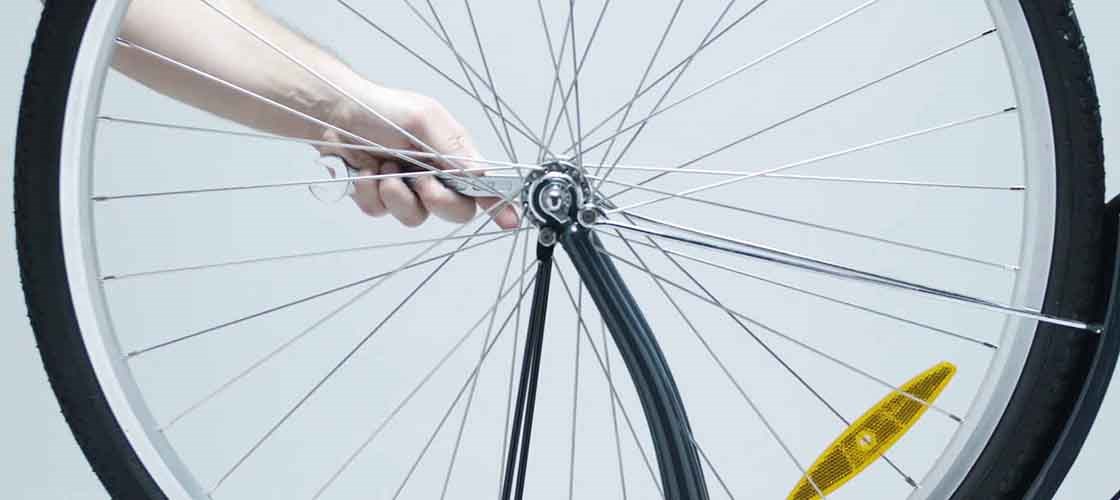 Close-up of a hand adjusting a bicycle wheel with a reflector on it.