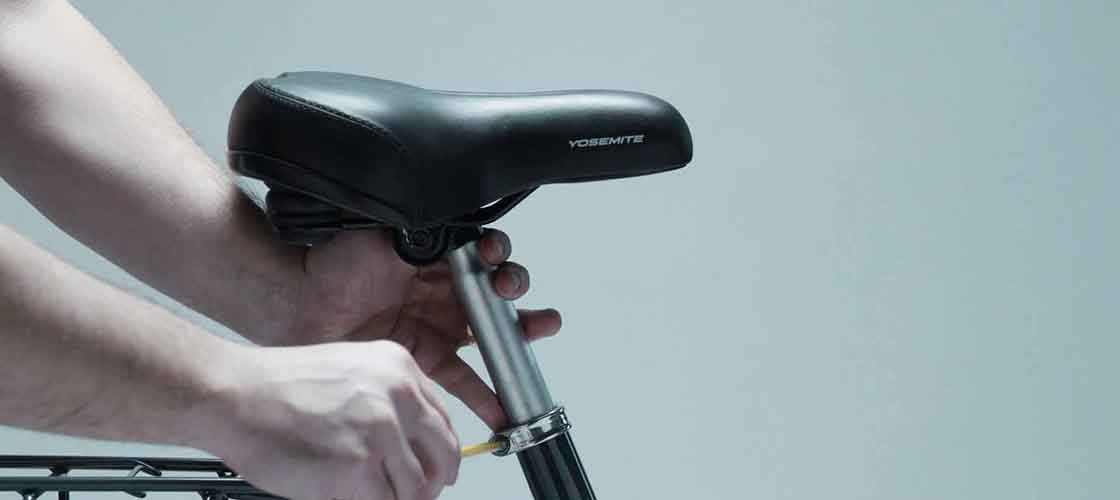 Close-up of a hand adjusting the height of a black bicycle saddle. The saddle says Yosemite in white letters.