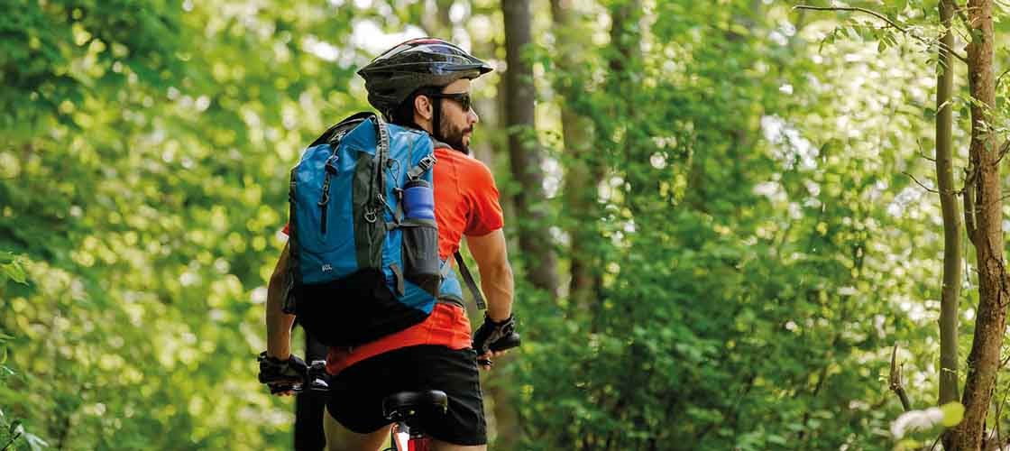A man rides a mountain bike in a forest environment. The man is equipped with a helmet and a backpack.